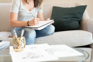 Woman sitting on white couch writing on notepad