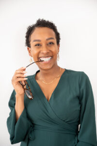 Woman is smiling at the camera holding her glasses playfully on her small business brand photoshoot